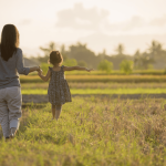 A woman walks through a field with her child.